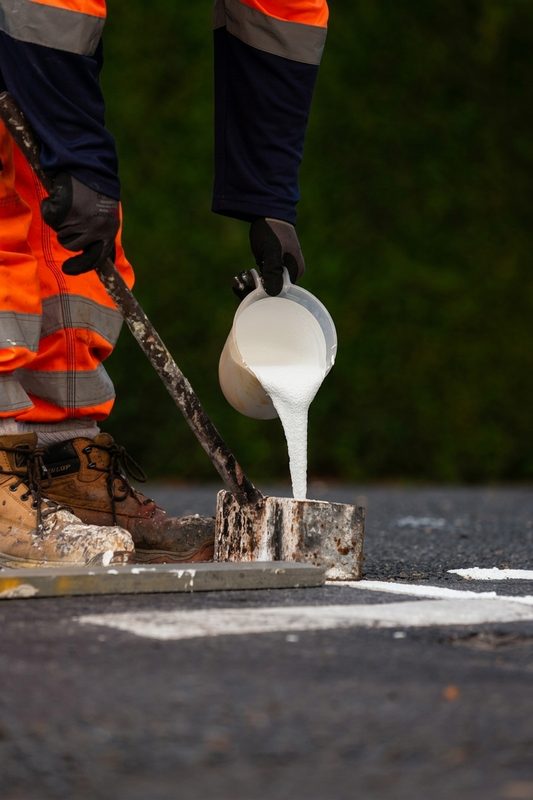 Close-up of a highway operative pouring white thermoplastic material into a mould for manual road marking.