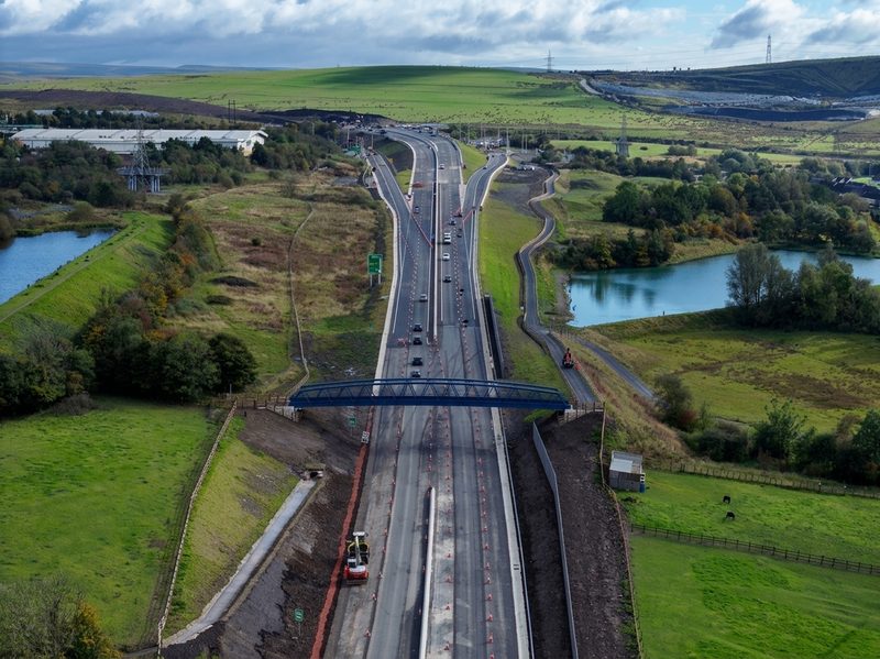 Drone view of a highway construction site featuring a new blue footbridge, traffic cones and road upgrade.