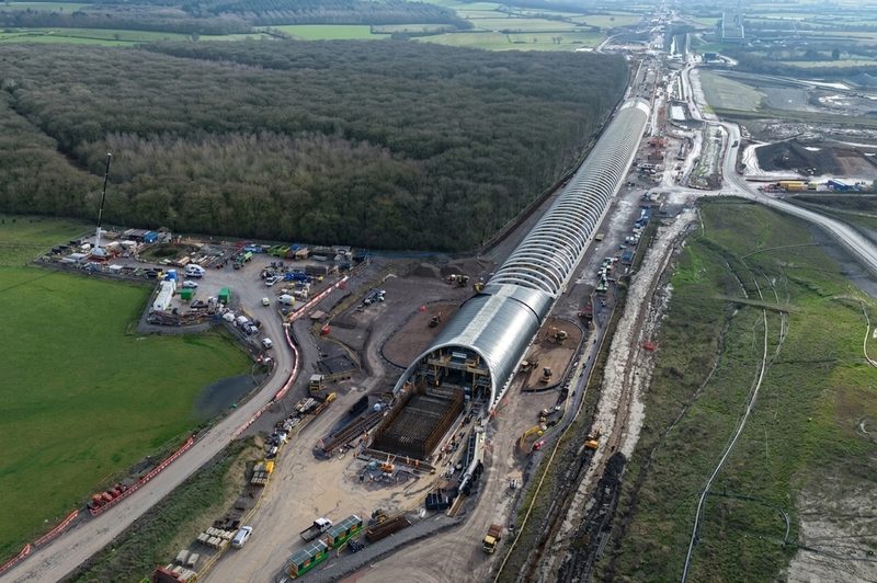 High-angle drone view of a curved steel bat mitigation structure under construction next to woodland.