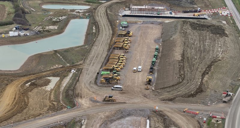 Aerial drone view of articulated dump trucks and earthmoving plant parked at a highway construction site depot.
