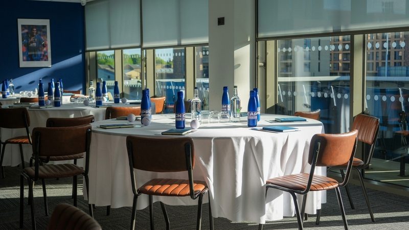 A corporate meeting room with round tables, branded water bottles and notebooks set up for an event.