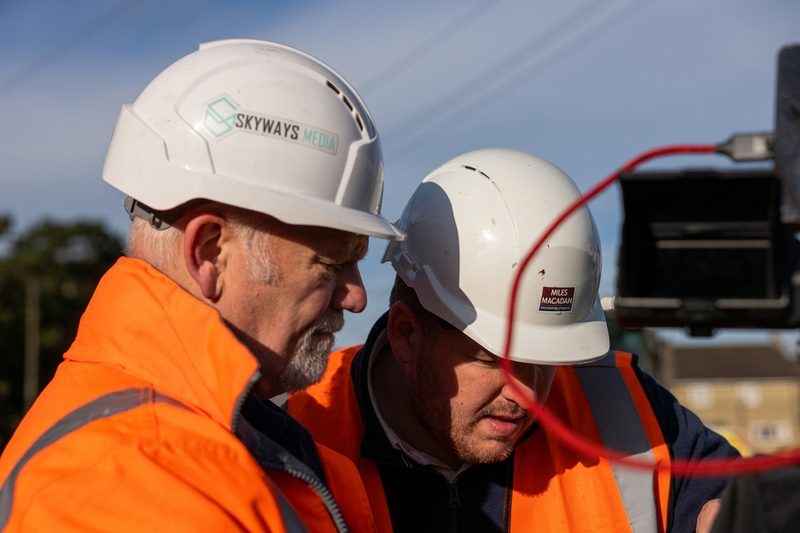 Two highway operatives in hi-vis clothing and hard hats review data on a screen at a site.