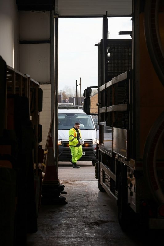 A highway operative in high-visibility clothing walks past a maintenance van outside a depot garage.