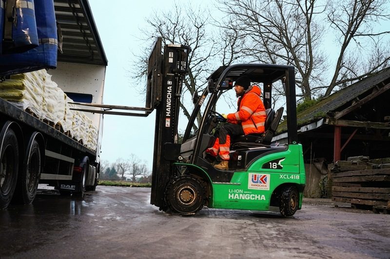 A green forklift loading white sandbags onto a heavy goods vehicle in a UK highways depot.