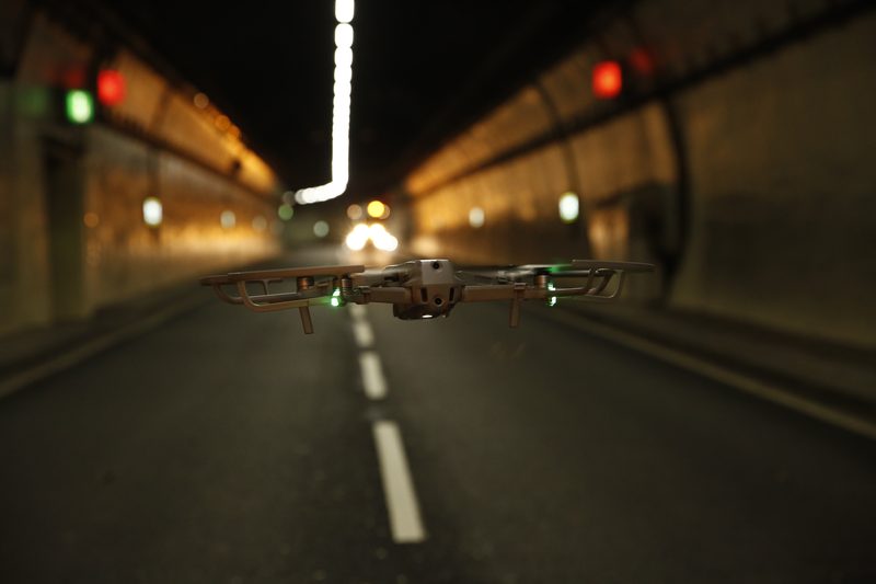 A drone with propeller guards flying through a highway tunnel at night with glowing green lights.