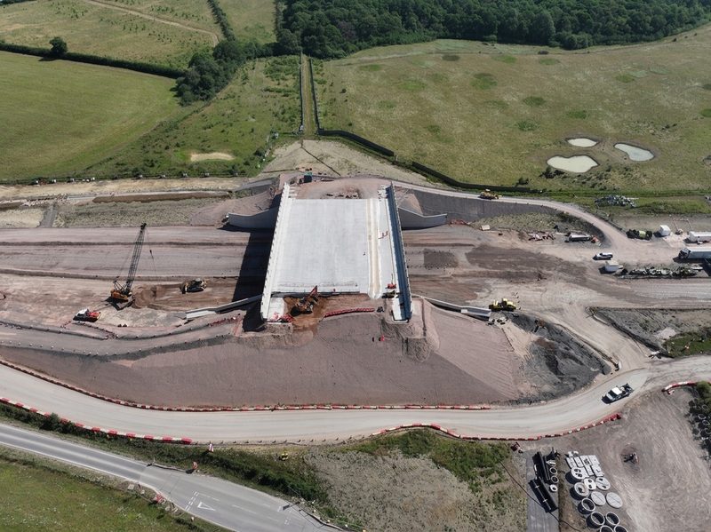 An aerial drone view showing a concrete bridge under construction with earthworks and heavy plant on site.