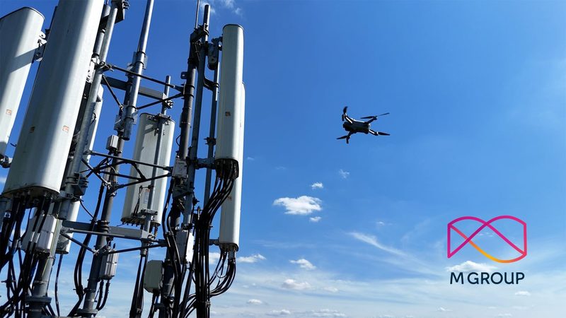 A video frame showing a drone surveying a telecommunications tower against a clear blue sky.