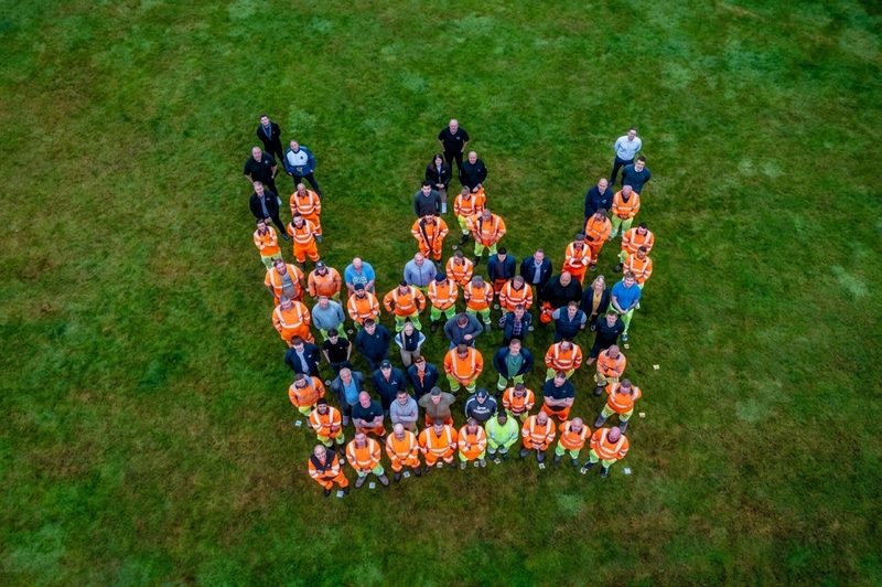 Aerial drone view of site operatives in orange hi-vis workwear forming a crown shape on a field.