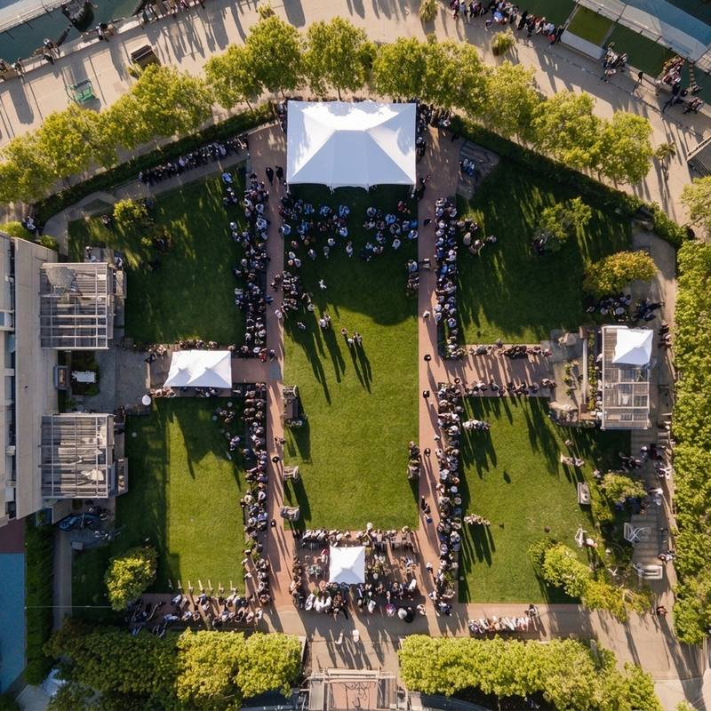 High-angle aerial view of a corporate outdoor event with guests gathered around marquees on a lawn.