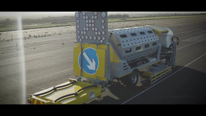 Video frame of an automated cone laying machine and impact protection vehicle on a highway test surface.