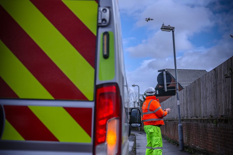 A hi-vis operative operates a drone to survey a lighting column next to a highways service vehicle.