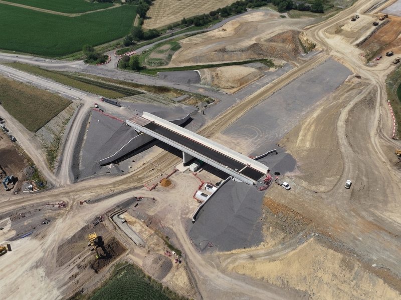 Drone view of a concrete bridge structure under construction surrounded by extensive earthworks and highway plant.