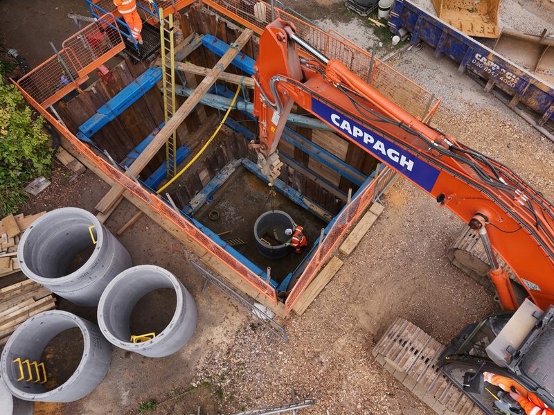 High-angle view of a sheet-piled excavation with an operative installing concrete rings and heavy plant machinery.