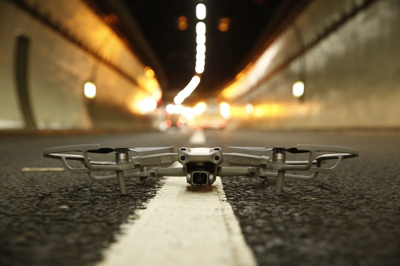 Close-up of a small drone with propeller guards positioned on a white road marking inside a tunnel.