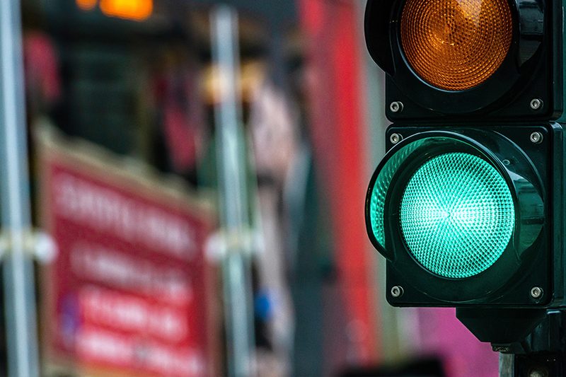 Close-up of a green traffic light signal at a UK roadworks site with blurred background signage.
