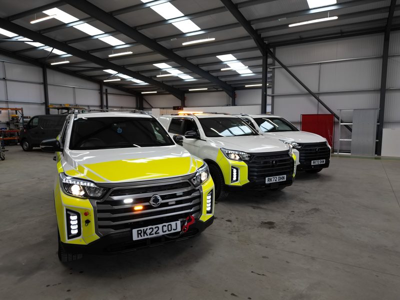 Three white and yellow highways fleet vehicles parked inside a large industrial depot with overhead lighting.