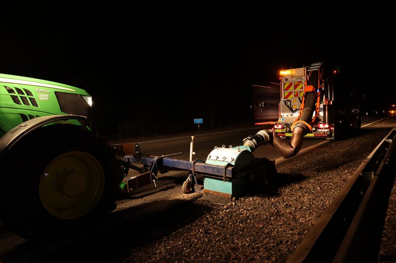 Specialist highway plant and a tractor performing road maintenance on a dark dual carriageway at night.