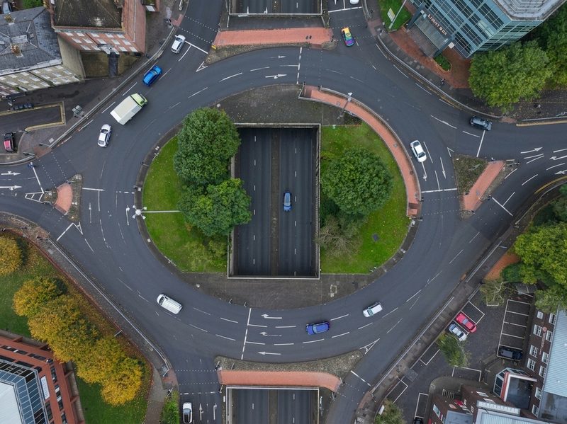 Aerial drone view of a large urban roundabout with a dual carriageway underpass and moving traffic.