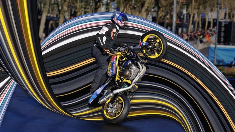 A stunt motorcyclist performing a wheelie with a colourful pixel stretch effect at a highways event.
