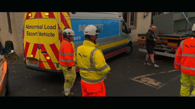 Video frame showing site staff and an abnormal load escort vehicle for a bridge installation project.