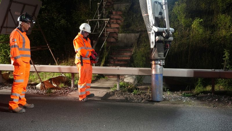 Operatives in hi-vis using a suction excavator for highway maintenance under artificial lighting during night works.