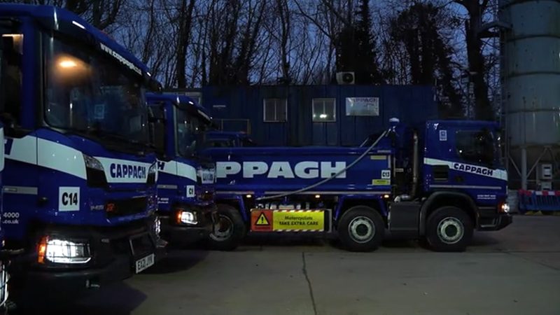 Video frame showing branded blue HGVs parked at a highway depot during low light hours.