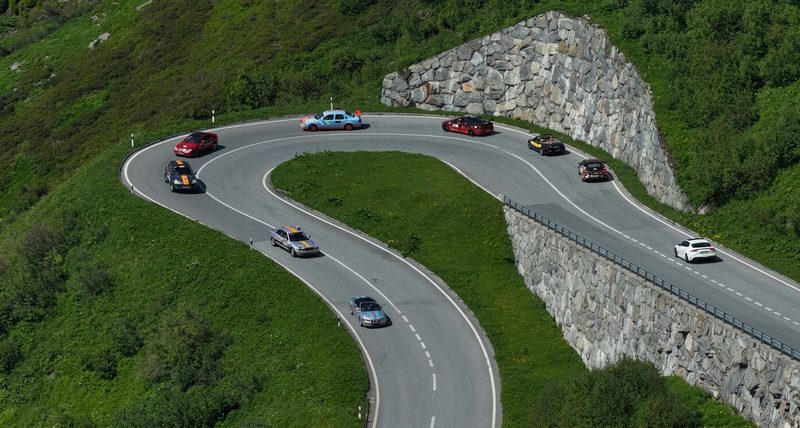 Aerial view of cars navigating a sharp hairpin bend on a mountain highway with large stone retaining walls.