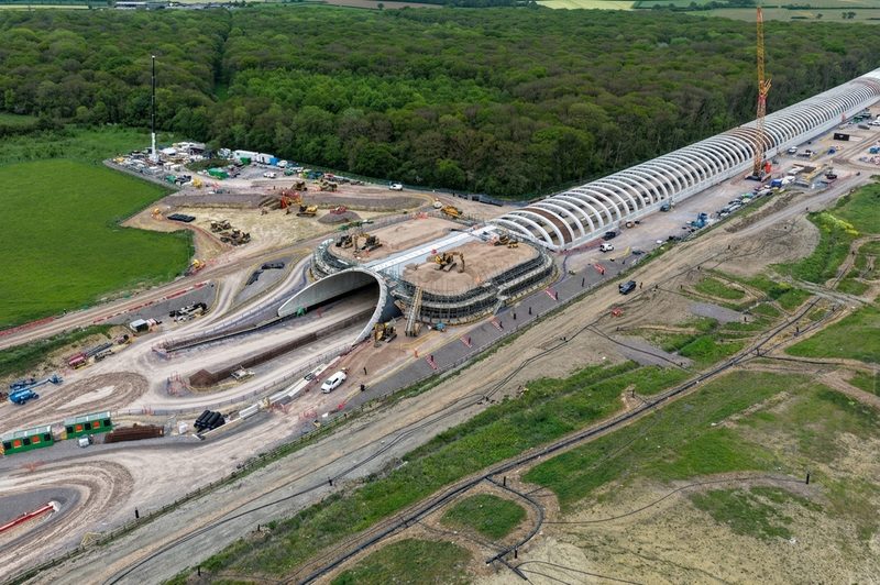 Aerial view of a large concrete tunnel portal and precast arch segments under construction.