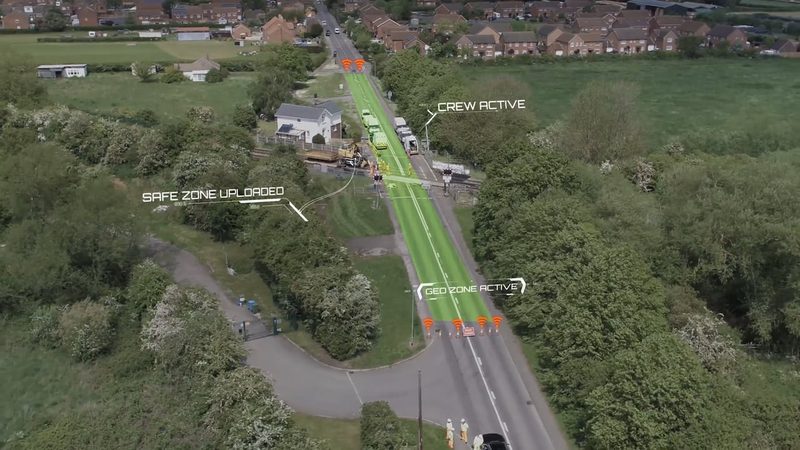Aerial video frame displaying digital geofencing overlays across a road and rail level crossing worksite.
