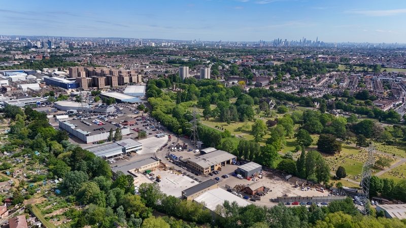 High-angle drone view of a highways depot and industrial units with the London skyline in the distance.
