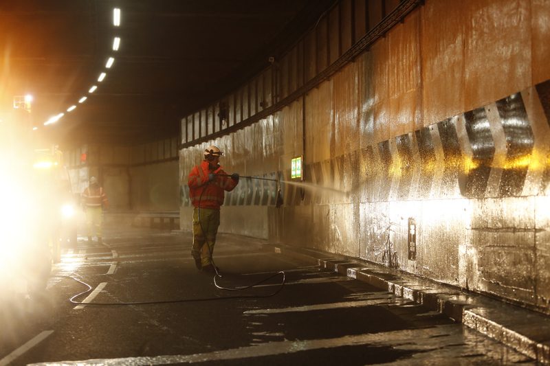 Highways operative in hi-vis using a high-pressure jet wash to clean a tunnel wall during night works.