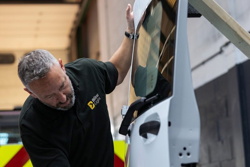 A maintenance technician inspecting a white vehicle door within a highway depot or workshop environment.