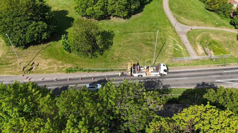 High-angle drone view of a traffic management vehicle and cones being placed along a rural road.