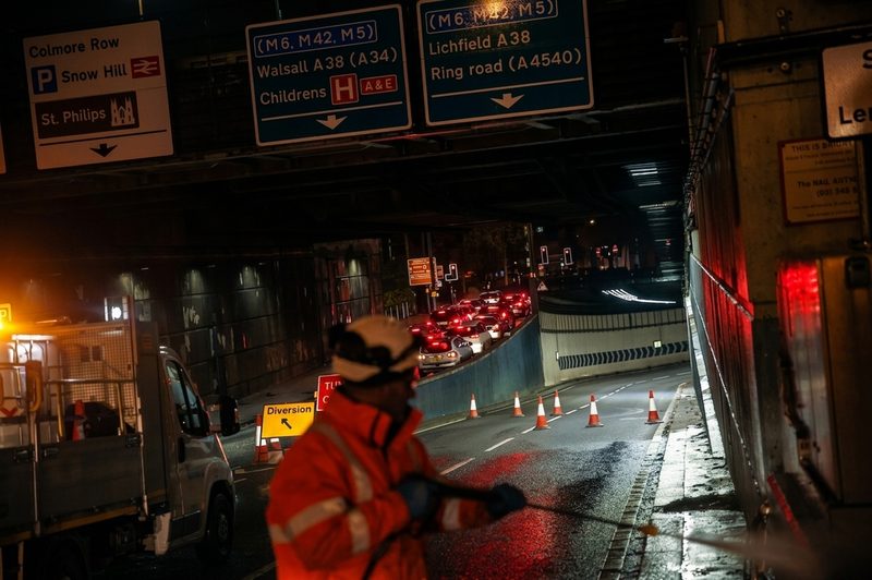 Highways operative working at night near a tunnel entrance with traffic cones and diversion signage visible.